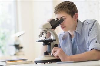 Teenage boy (16-17) looking through microscope.