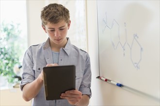 Teenage boy (16-17) using digital tablet in classroom.
