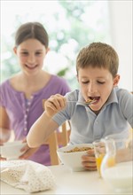 Boy and girl (8-9, 10-11) eating cereals.