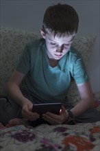 boy (8-9) using digital tablet in bed.