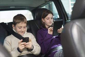 Boy and girl (8-9, 10-11) using digital tablet and smart phone in car.