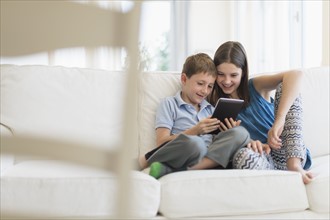Boy and girl (8-9, 10-11) sitting on sofa using digital tablet.