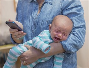 Woman texting and holding crying baby boy (2-5 months).