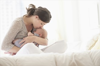 Mother kissing baby boy (2-5 months) in bed.