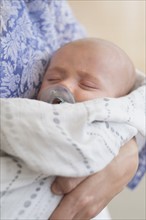 Close up of baby boy (2-5 months) sleeping in mother's arms.