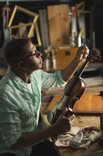 Mature man fixing violin in his workshop.