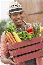 Portrait of man carrying crate full of fresh vegetables.