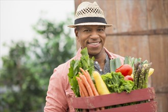 Portrait of man carrying crate full of fresh vegetables.