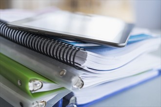 Close up of stack of notebooks with digital tablet on top.