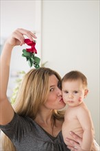 Mother holding baby girl (6-11 months) and mistletoe.
Photo : Jamie Grill