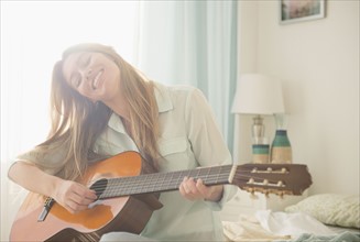 Young woman playing acustic guitar on bed.
Photo : Jamie Grill