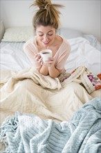 Young woman sitting in bed with coffee.
Photo : Jamie Grill