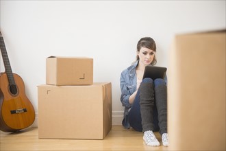 Young woman sitting on floor with digital tablet with boxes around her.
Photo : Jamie Grill