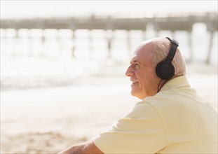 Senior man with headphones sitting on beach.
Photo : Daniel Grill