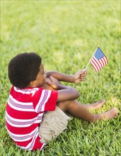 boy (6-7) sitting on grass and holding american flag.
Photo : Daniel Grill