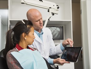 Dentist holding digital tablet with patient's x-ray.