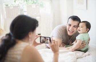 Mother photographing father with baby son (6-11 months) in bedroom.