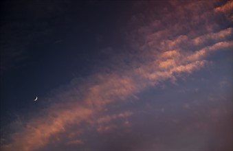 Moon against cloudy sky at sunset.