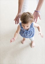 Mother assisting baby daughter (18-23 months) with her first steps.