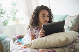 Girl (8-9) using digital tablet on bed.