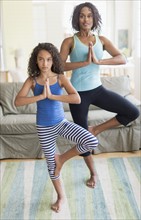 Mother and daughter (8-9) doing in yoga poses in living room.