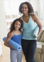 Mother and daughter (8-9) holding yoga mats in living room.