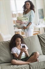 Girl (8-9) text messaging on sofa, mother in background.