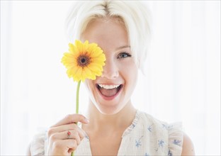 Portrait of blonde woman holding yellow flower.