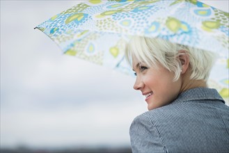 Profile of blonde woman under umbrella.