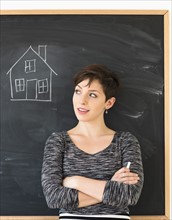 Woman in front of blackboard with house drawing.