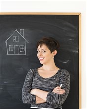 Woman in front of blackboard with house drawing.