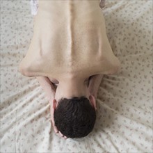 Elevated view of shirtless woman bending on bed.