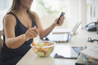 Woman working in home office and eating salad.