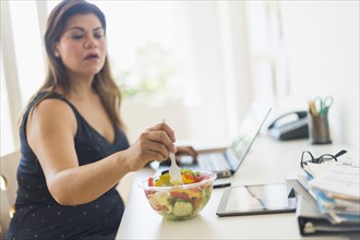 Woman eating salad and using laptop in office.