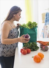 Woman taking out vegetables of grocery bag.