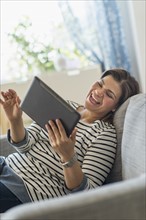 Portrait of happy woman lying on sofa with tablet pc.