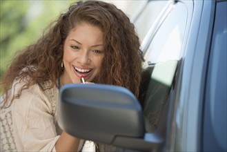 Young woman putting lipstick looking at rear mirror.