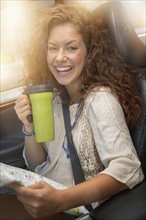 Woman sitting in car with map and disposable cup.