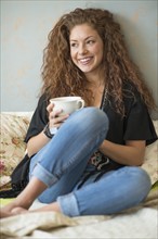 Portrait of woman sitting on bed with tea cup.