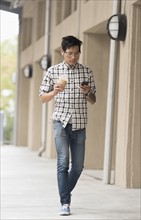 Man walking on sidewalk with iced coffee and mobile phone.