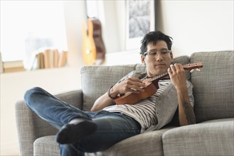Man sitting on sofa and playing ukulele.