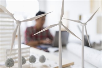 Wind turbine models on desk, architect in background.