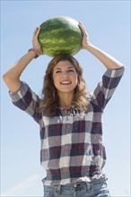 Young woman carrying on head watermelon.