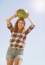Young woman carrying on head watermelon.