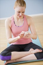 Young woman using mobile phone sitting on exercise mat