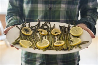 Man holding platter with asparagus and lemon