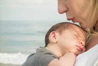 Mother holding newborn daughter on beach