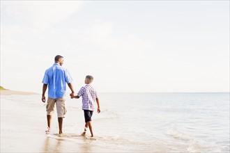 Father and son (10-11) walking on beach