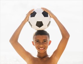 Boy (10-11) holding soccer ball on head