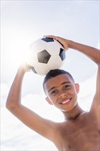 Boy (10-11) holding soccer ball on head